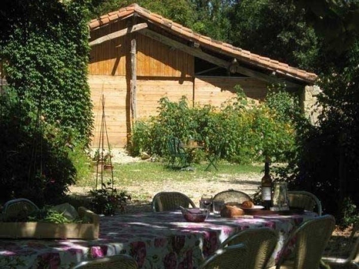 Location de vacances - Maison - Villa à Castéra-Verduzan - la table des repas sous les arbres, au fond la grange avec la cuisine d'été